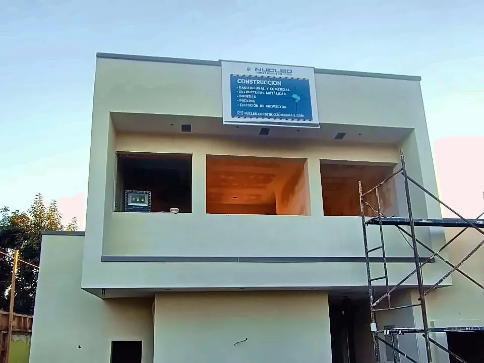 Casa de dos pisos en construcción, con andamio y el letrero de Núcleo Construcción