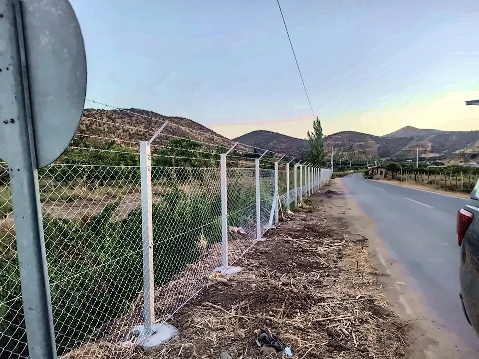 Cierro perimetral con postes y malla junto a un camino rural