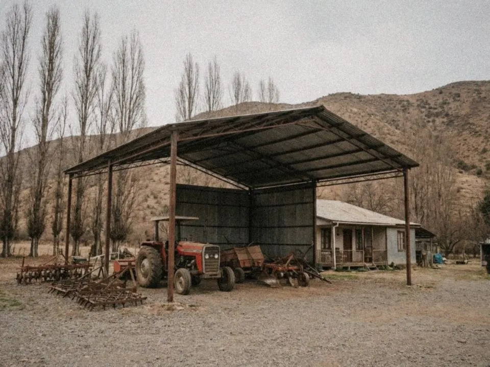 Cobertizo metálico abierto que resguarda un tractor y maquinaria agrícola