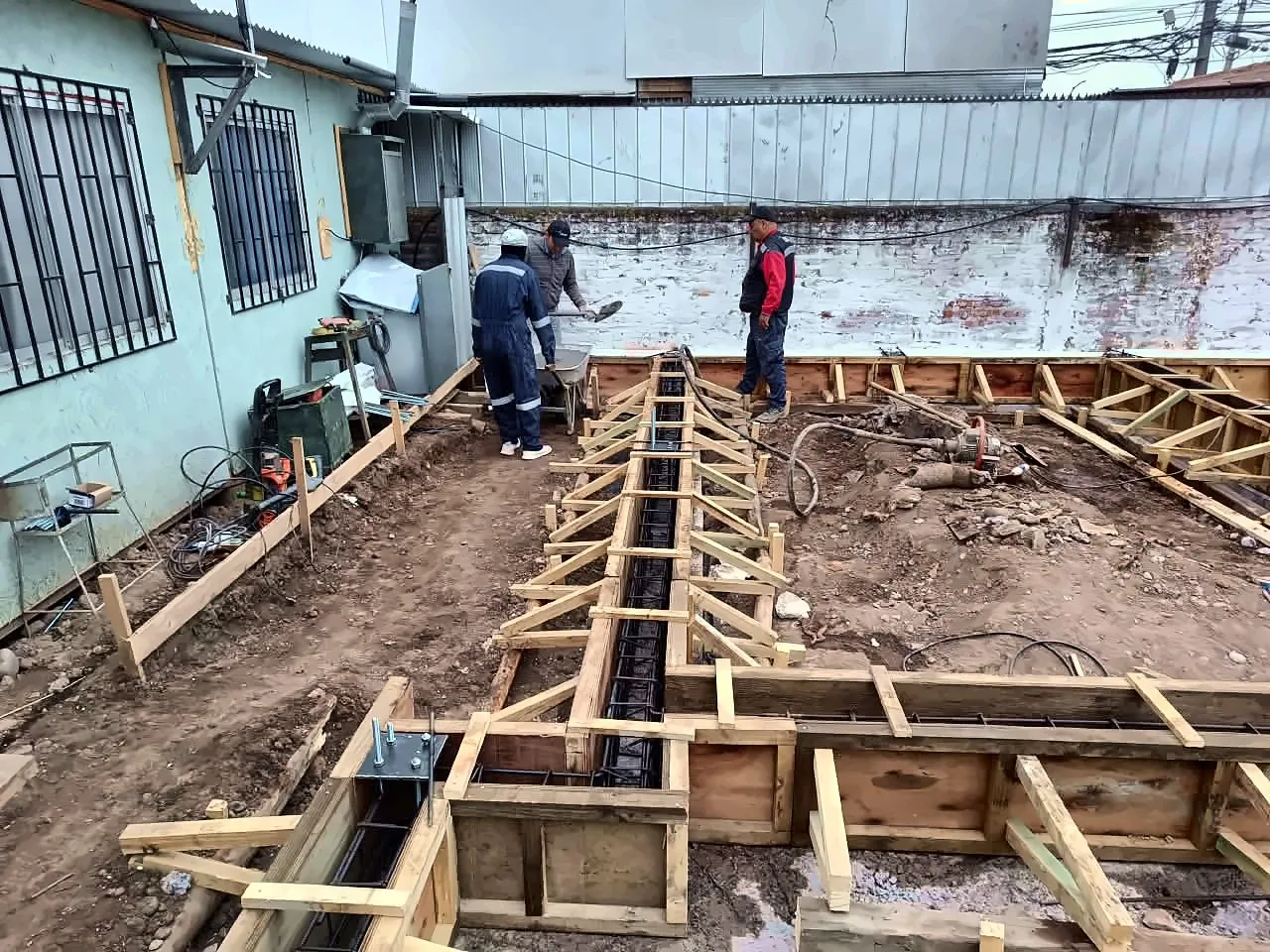 Equipo de Núcleo Construcción armando moldajes y enfierradura de una fundación junto a una casa