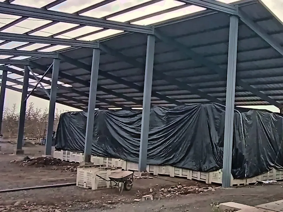 Estructura metálica de un galpón en montaje, con la carga cubierta por un manto negro